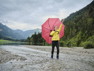 Mädchen mit Regenschirm spritzt Wasser am Seeufer - DIKF00653