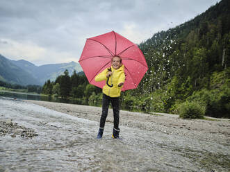 Glückliches Mädchen mit Regenschirm genießt das Plätschern des Wassers am Seeufer - DIKF00654