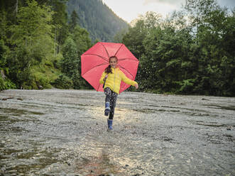 Glückliches Mädchen, das einen Regenschirm hält und im See Wasser spritzt - DIKF00657