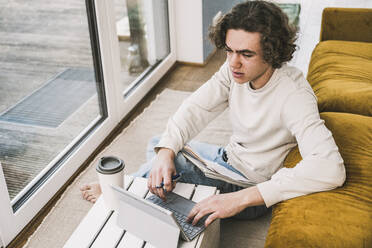 Junger Mann mit Tablet-PC beim Lernen im heimischen Wohnzimmer - UUF25537