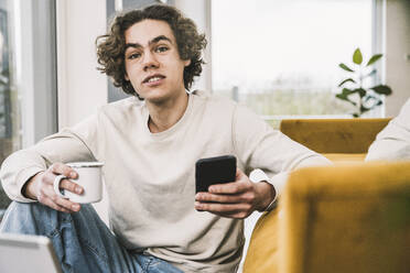 Young man with coffee cup and smart phone at home - UUF25540