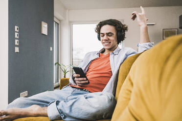 Glücklicher Mann hört Musik über drahtlose Kopfhörer mit seinem Smartphone auf dem Sofa zu Hause - UUF25551