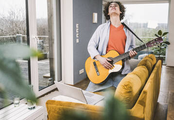 Junger Mann spielt Gitarre und lernt mit Hilfe eines Online-Tutorials am Laptop zu Hause - UUF25560