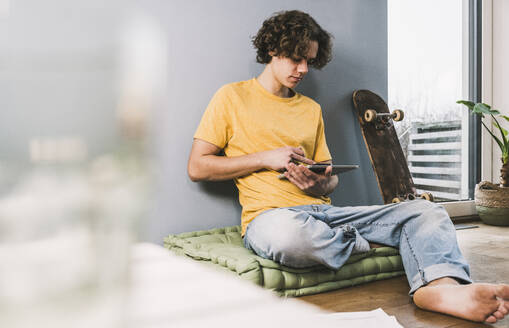 Junger Mann benutzt Tablet-PC mit Skateboard zu Hause - UUF25566