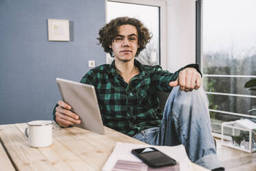 Junger Mann mit Tablet-PC sitzt am Tisch im Wohnzimmer - UUF25575
