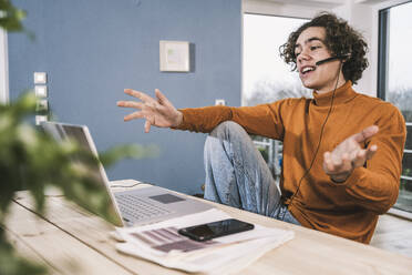 Young man gesturing E-learning through laptop at home - UUF25585