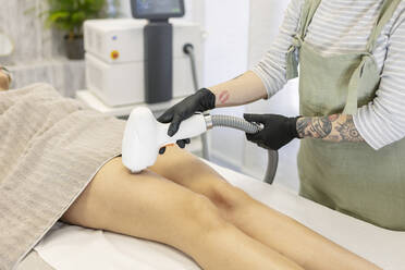 Therapeut entfernt in einer Schönheitsklinik mit einem Lasergerät Haare vom Bein einer Frau - MTBF01182