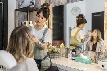 Kosmetikerin trägt Make-up auf das Gesicht einer Frau im Salon auf - MTBF01190