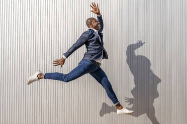 Excited businessman with hand raised jumping by white wall - DLTSF02663
