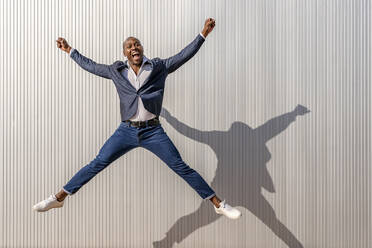 Happy businessman with mouth open jumping in front of white wall - DLTSF02664