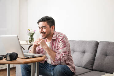 Happy freelancer with hands clasped attending video call through laptop at home - FLMF00787