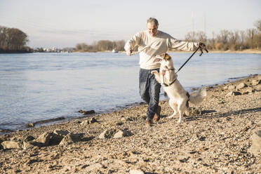 Glücklicher älterer Mann läuft mit Hund am Strand - UUF25598