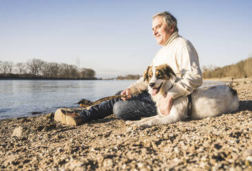 Lächelnder Mann mit Stock und Hund am Strand an einem sonnigen Tag - UUF25599