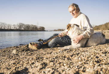 Älterer Mann im Gespräch mit Hund am Flussufer an einem sonnigen Tag - UUF25600
