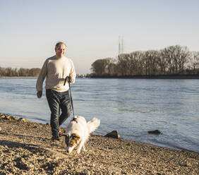 Glücklicher älterer Mann mit Hund beim Spaziergang am Strand - UUF25601