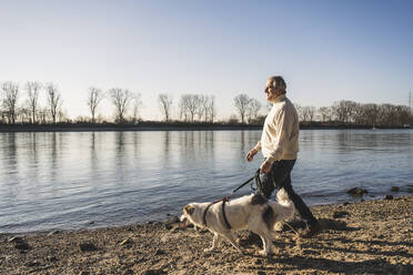 Mann geht mit Hund am Strand spazieren - UUF25602