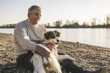 Happy senior man looking at pet dog on sunny day - UUF25614