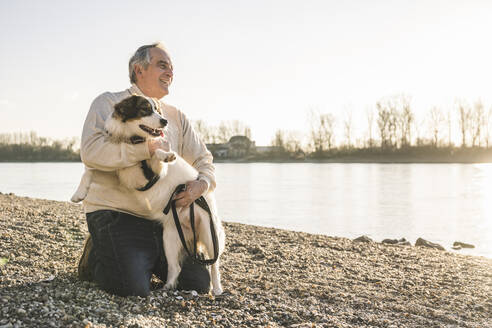 Glücklicher älterer Mann umarmt Hund am Strand an einem sonnigen Tag - UUF25616