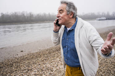Senior man talking on smart phone at beach - UUF25646