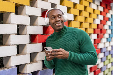 Lächelnder Mann, der ein Mobiltelefon an einer bunten Wand hält - DLTSF02708