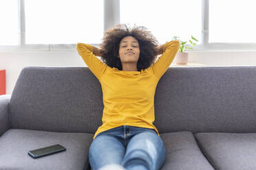 Young woman with hands behind head relaxing on sofa at home - XLGF02694