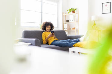 Lächelnde Frau mit Smartphone sitzt auf dem Sofa im Wohnzimmer zu Hause - XLGF02696