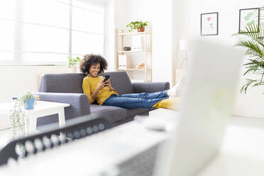 Smiling woman surfing net through mobile phone in living room - XLGF02697