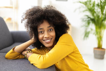 Smiling young woman leaning on sofa sitting in living room - XLGF02706
