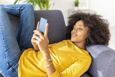 Junge Frau benutzt ihr Smartphone und entspannt sich auf dem Sofa zu Hause - XLGF02709