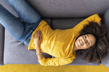 Smiling young woman lying on sofa at home - XLGF02711