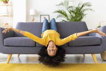 Glückliche junge Frau liegt kopfüber auf dem Sofa im Wohnzimmer zu Hause - XLGF02712