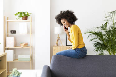 Fröhliche Frau spricht mit ihrem Smartphone auf dem Sofa im Wohnzimmer - XLGF02715
