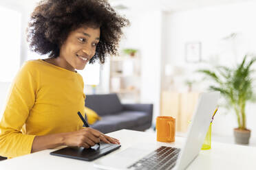 Glückliche junge Frau, die zu Hause mit einem digitalisierten Stift auf einem Tablet-PC schreibt - XLGF02720