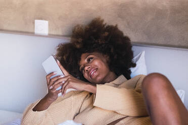 Junge Frau mit Smartphone auf dem Bett liegend zu Hause - PNAF03094