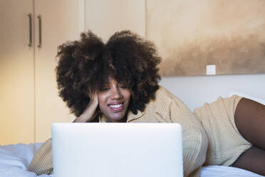 Woman using laptop lying on bed at home - PNAF03117