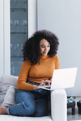 Frau mit Laptop auf dem Sofa im Wohnzimmer sitzend - PNAF03152