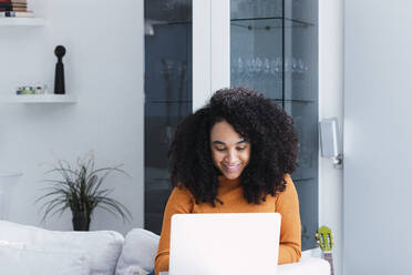 Smiling woman using laptop at home - PNAF03153