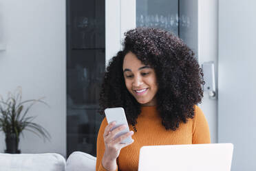 Frau mit Laptop und Smartphone im Wohnzimmer - PNAF03154