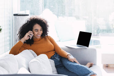 Smiling woman talking on mobile phone in living room - PNAF03155