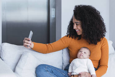 Mother with baby boy taking selfie on smart phone in living room - PNAF03161