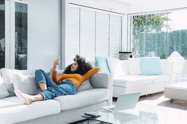 Woman using smart phone lying on sofa in living room - PNAF03188