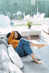 Frau mit Smartphone auf Sofa im Wohnzimmer liegend zu Hause - PNAF03191