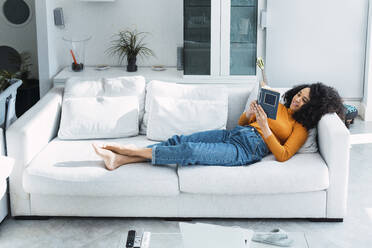 Frau liest ein Buch auf dem Sofa im Wohnzimmer zu Hause - PNAF03192