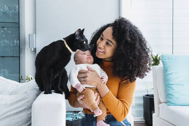 Lächelnde Mutter mit einem kleinen Jungen, der eine Katze im Wohnzimmer betrachtet - PNAF03195