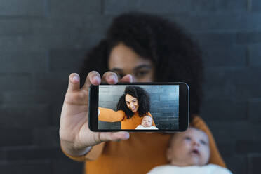 Mother taking picture with son on smart phone in front of wall - PNAF03207