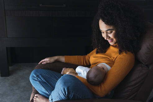 Lächelnde Mutter, die ihren kleinen Jungen zu Hause stillt - PNAF03212