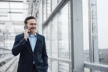 Smiling businessman talking on mobile phone in greenhouse - MOEF03977