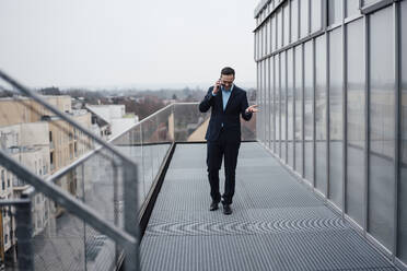 Glücklicher Geschäftsmann, der mit seinem Handy telefoniert und auf einem Balkon spazieren geht - MOEF04018