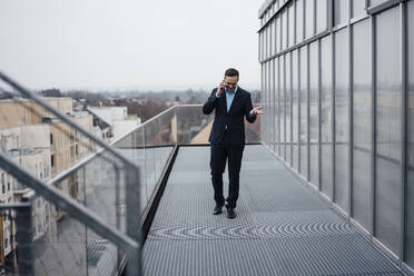 Happy businessman talking on mobile phone walking on balcony - MOEF04018