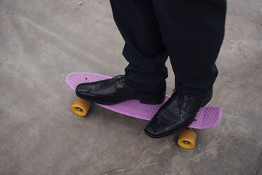 Beine eines Geschäftsmannes, der auf einem Skateboard steht - MOEF04025